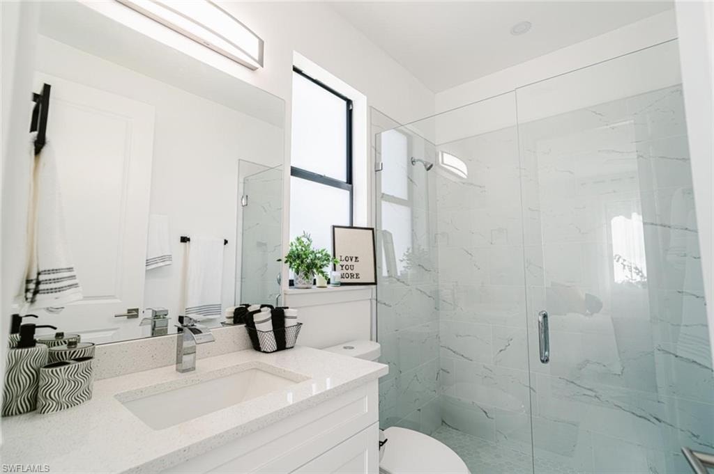 Contemporary bathroom featuring a spacious glass-enclosed shower with marbled wall tile, a white vanity with an integrated sink, a wide quartz countertop, and modern chrome fixtures