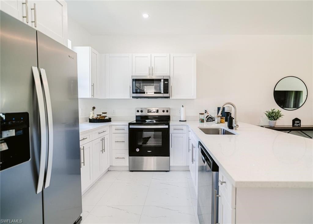 Kitchen featuring white shaker cabinetry, stainless steel appliances, light-toned countertops, a stainless steel sink with a gooseneck faucet, and large format floor tiling