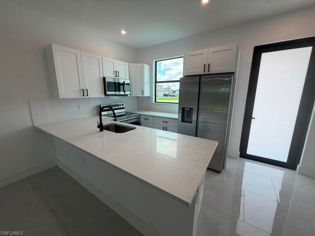 Modern kitchen featuring white shaker cabinetry, stainless steel appliances, a white subway tile backsplash, and light-toned countertops
