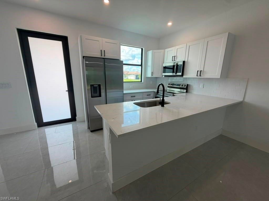 Modern kitchen featuring white shaker cabinetry, stainless steel appliances, a center island with countertop seating, and light-toned tile flooring