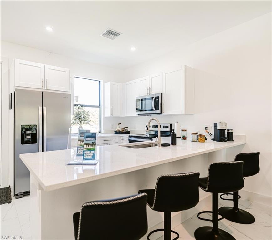 White kitchen featuring ample cabinetry, stainless steel appliances, a large island with seating, and light-colored countertops