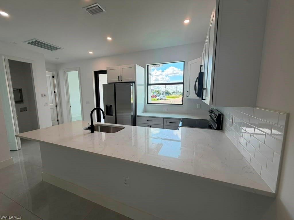 Kitchen featuring a large central island with a sink, white cabinetry, integrated stainless steel appliances, white subway tile backsplash, and recessed lighting