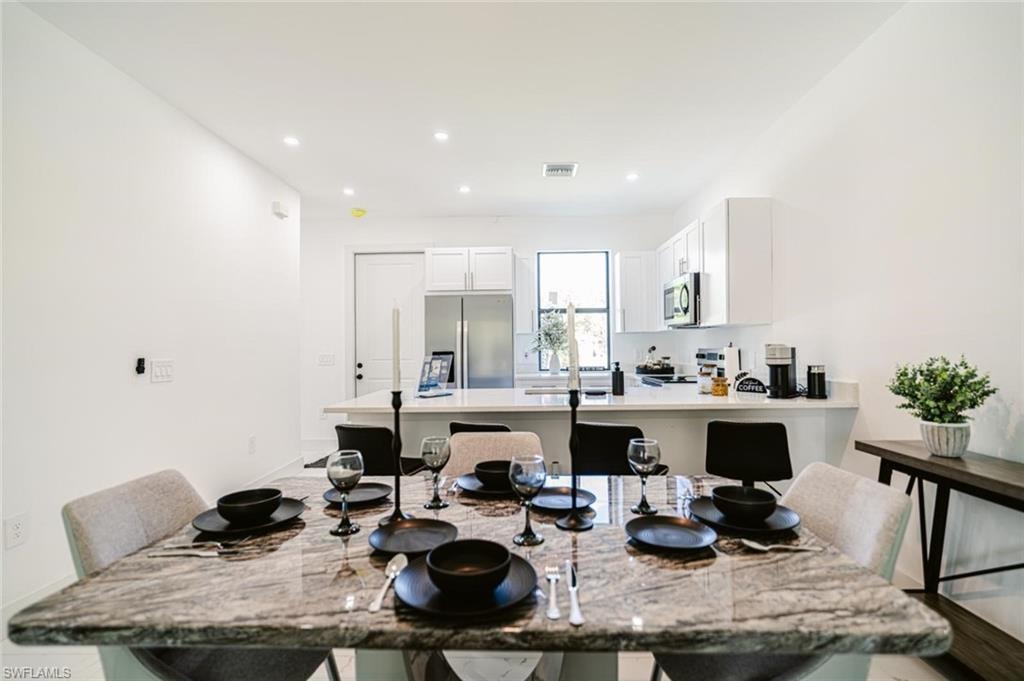 Spacious dining area with a polished stone-finish table, recessed lighting, and bright white walls
