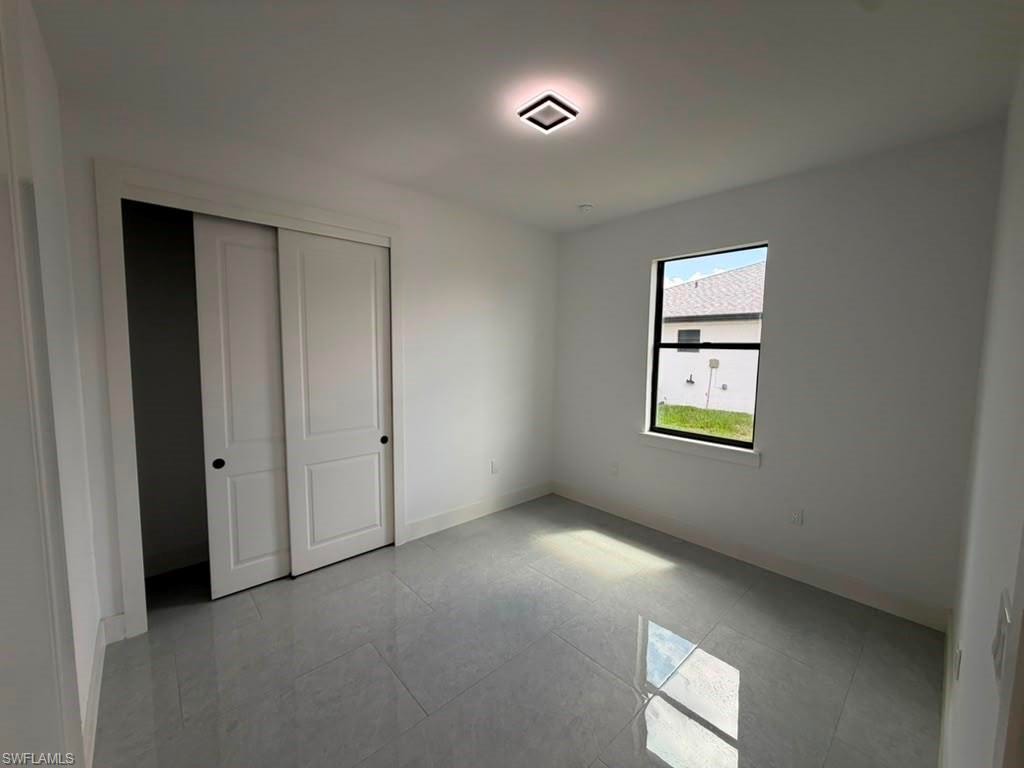 Bright room featuring a single window, a flush-mount ceiling light fixture, and a closet with bi-fold doors, all set on light-toned tile flooring