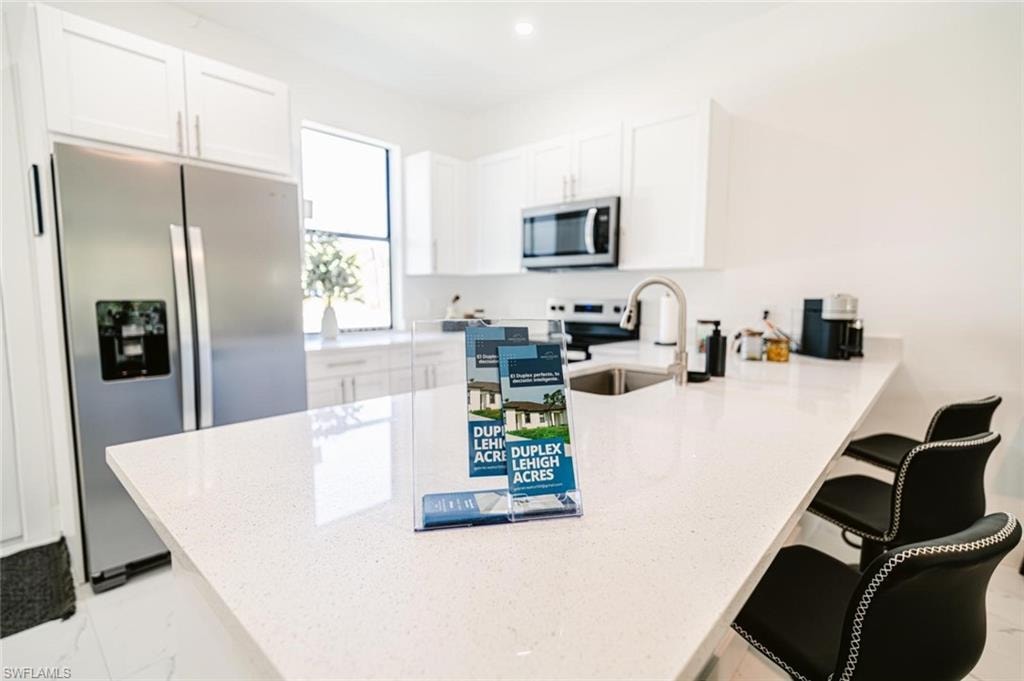 Modern kitchen featuring a large white countertop island with integrated sink, stainless steel appliances, white cabinetry, and recessed lighting