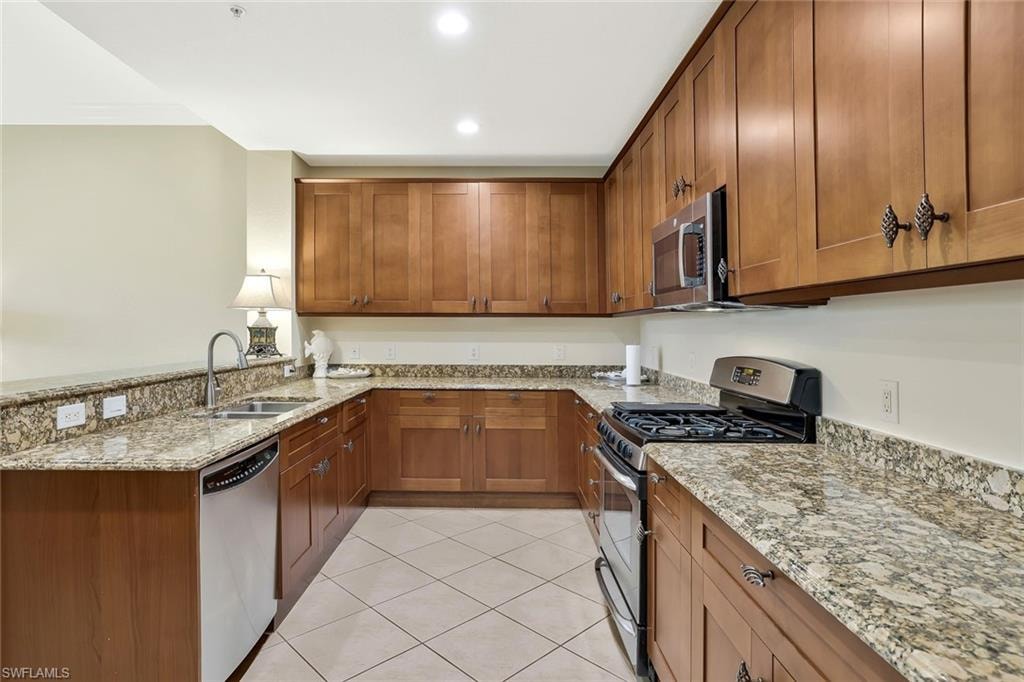 Kitchen featuring stainless steel appliances, brown cabinets, a peninsula, light tile patterned flooring, and recessed lighting