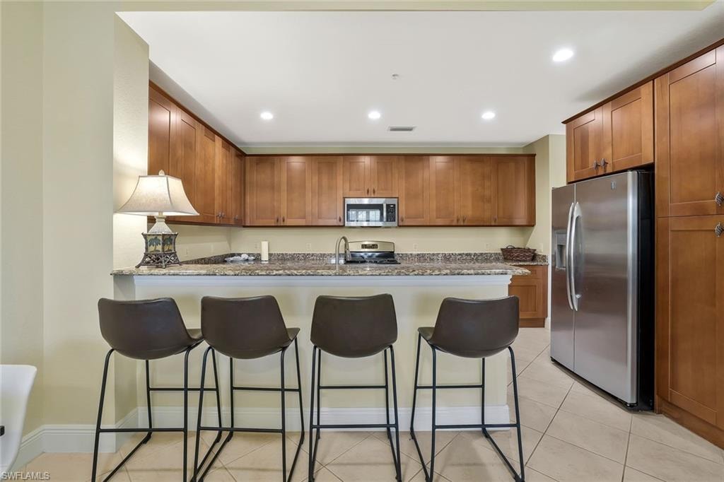 Kitchen with appliances with stainless steel finishes, recessed lighting, a peninsula, light tile patterned floors, and a kitchen bar