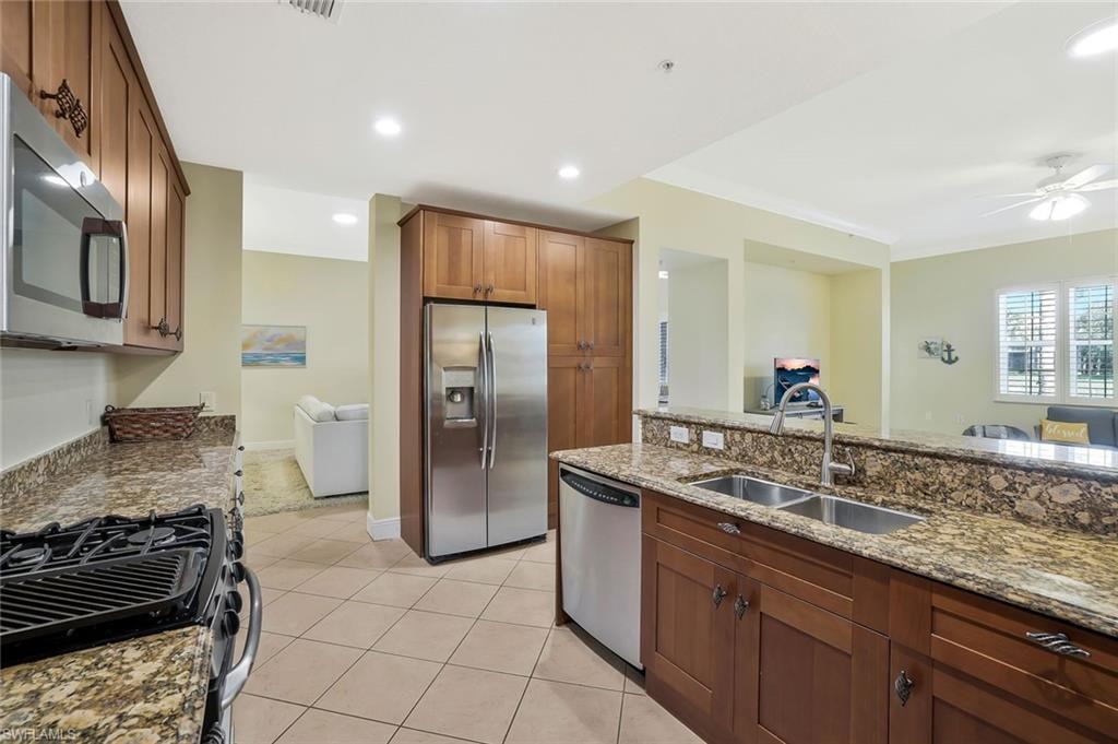 Kitchen with appliances with stainless steel finishes, light tile patterned flooring, ornamental molding, stone counters, and a ceiling fan