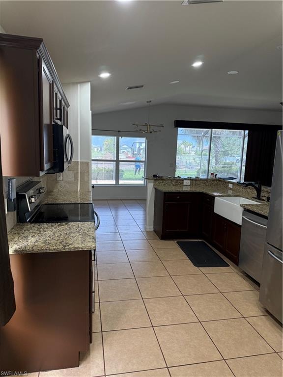 Kitchen featuring dark wood cabinetry, granite countertops, tile flooring, stainless steel appliances, and a farmhouse sink