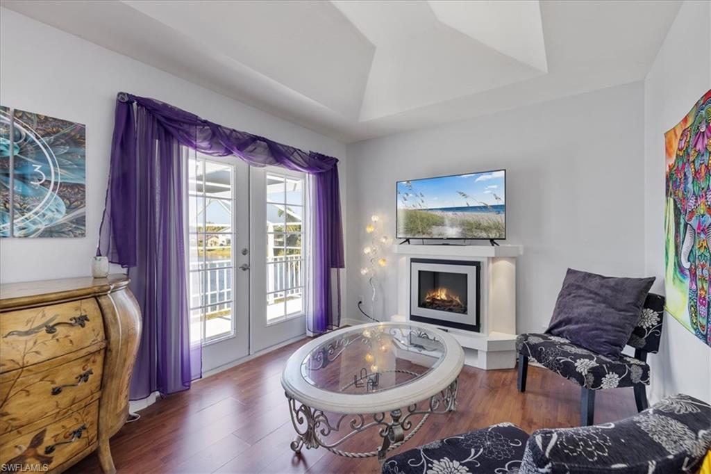 Living area featuring french doors, a warm lit fireplace, a raised ceiling, and wood finished floors