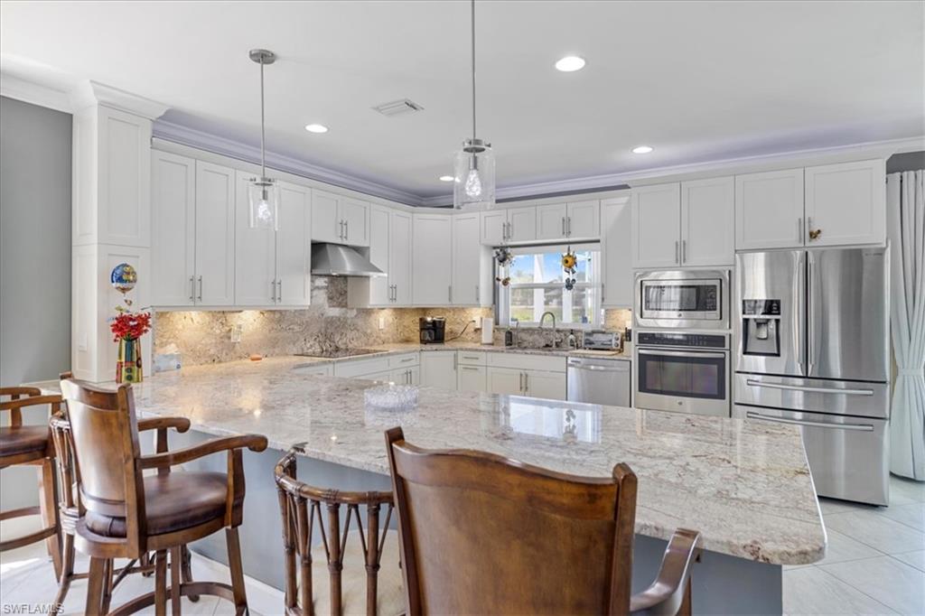 Kitchen with a sink, appliances with stainless steel finishes, a peninsula, under cabinet range hood, and visible vents