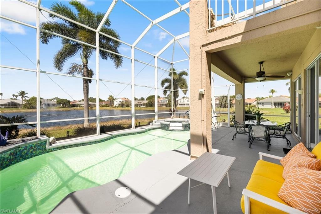 View of patio / terrace featuring glass enclosure, a water view, a pool with connected hot tub, and a ceiling fan