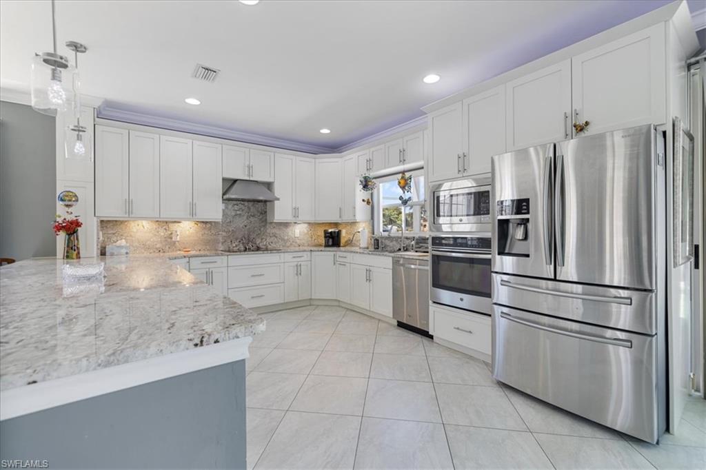 Kitchen with a peninsula, stainless steel appliances, under cabinet range hood, light stone counters, and backsplash