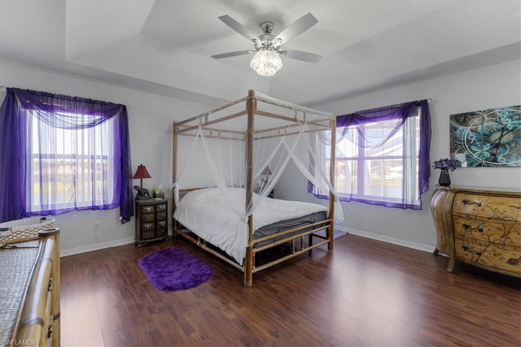 Bedroom with a ceiling fan, a tray ceiling, baseboards, and wood finished floors