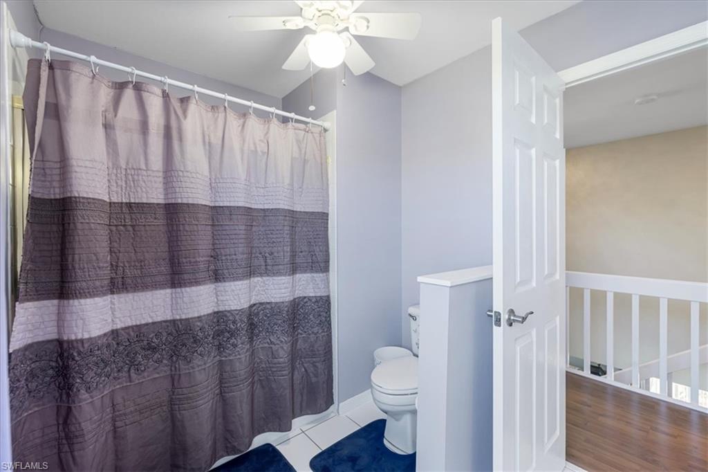 Full bathroom featuring tile patterned floors, toilet, curtained shower, baseboards, and ceiling fan