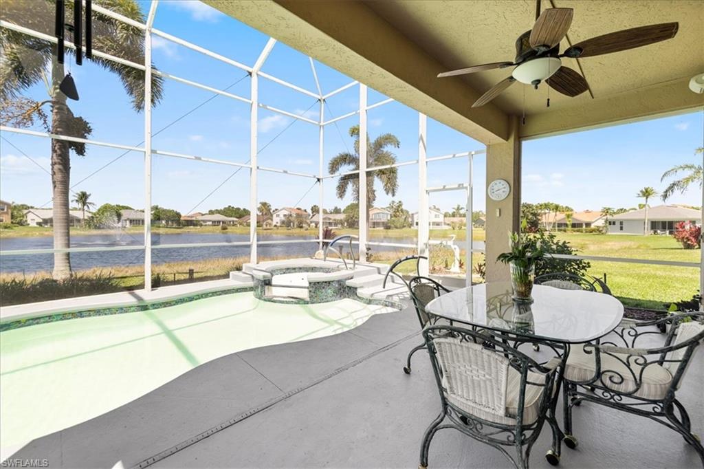 View of patio featuring a pool with connected hot tub, a ceiling fan, a lanai, outdoor dining space, and a water view