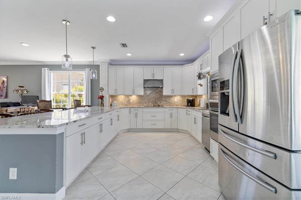 Kitchen with stainless steel refrigerator with ice dispenser, under cabinet range hood, decorative backsplash, visible vents, and a peninsula