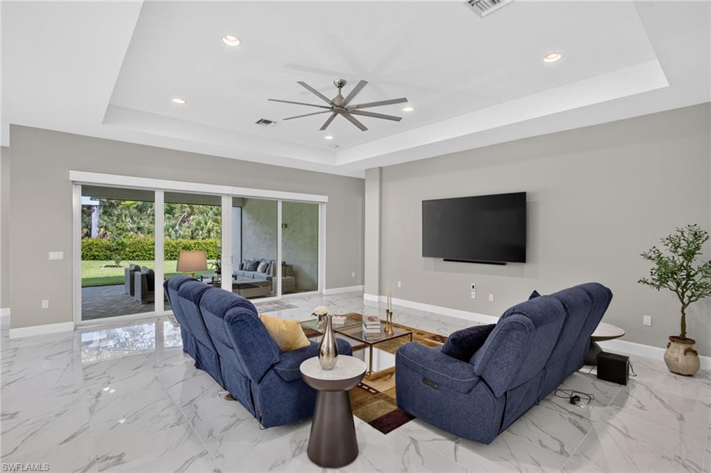 Spacious living area featuring large format white tile flooring, tray ceiling with recessed lighting, and expansive sliding glass doors opening to the exterior patio