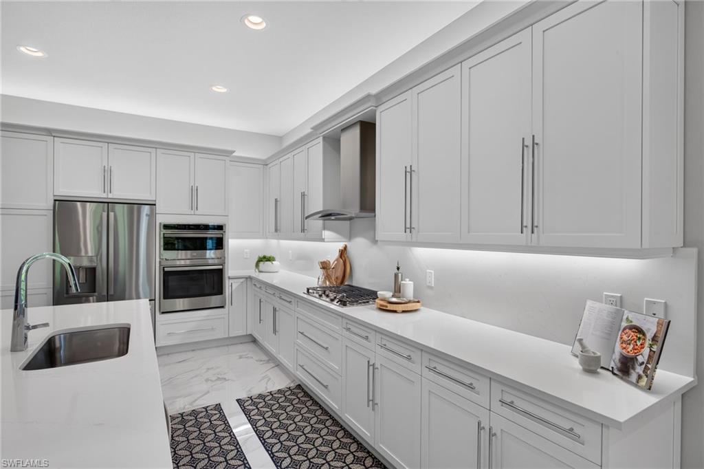 White shaker cabinetry with modern hardware, stainless steel appliances, marble-look tile flooring, undermount sink, and recessed lighting