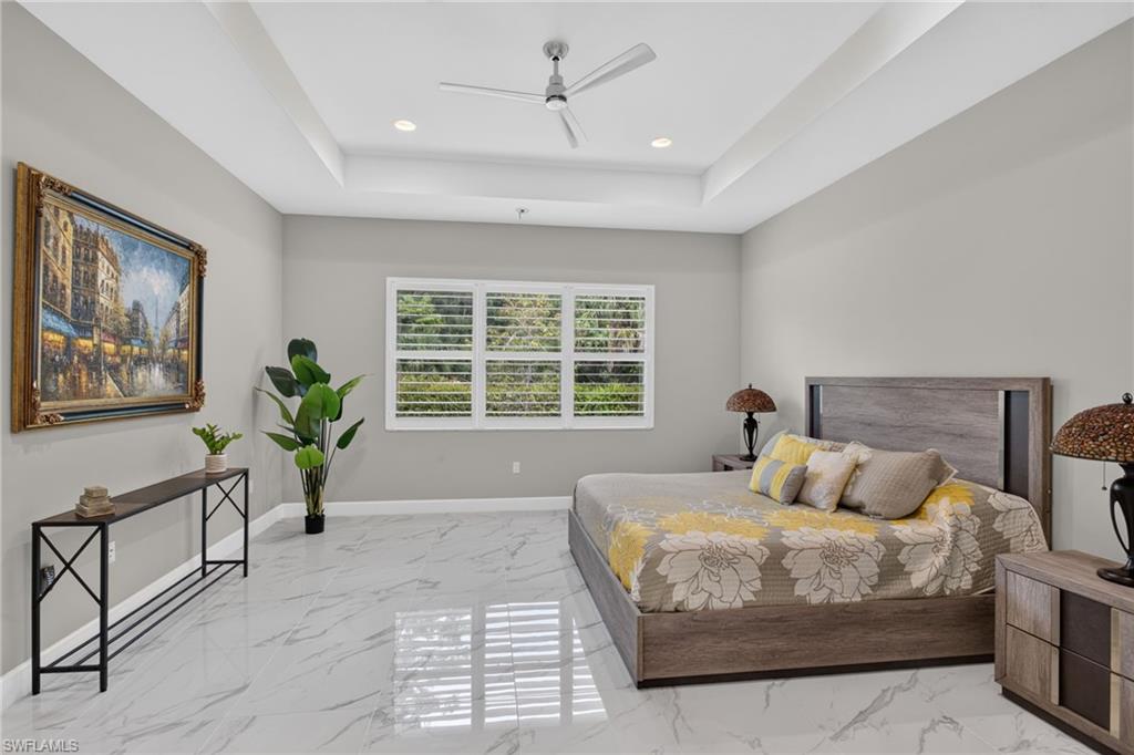 Spacious room featuring large format marble-look tile flooring, a tray ceiling with recessed lighting, and a modern ceiling fan