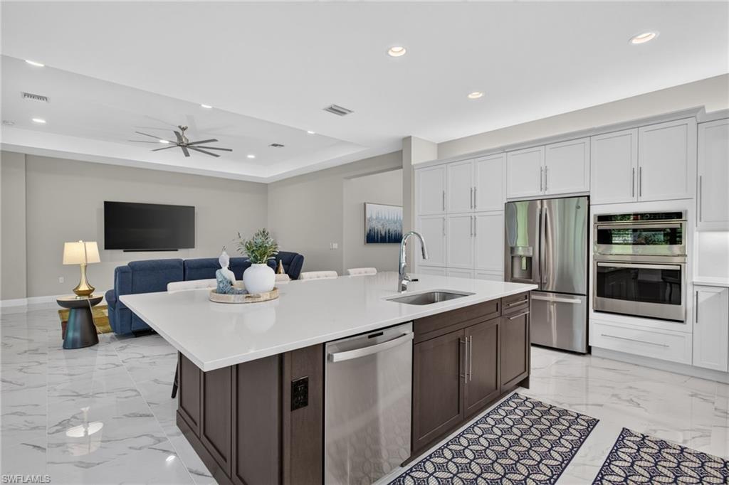 Open-concept kitchen featuring a large central island with integrated sink and dishwasher, white countertops, and stainless steel appliances