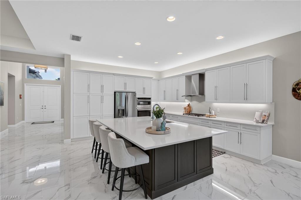 Gourmet kitchen featuring a large central island with a solid surface countertop, extensive white cabinetry, stainless steel appliances, and large format marble-look tile flooring