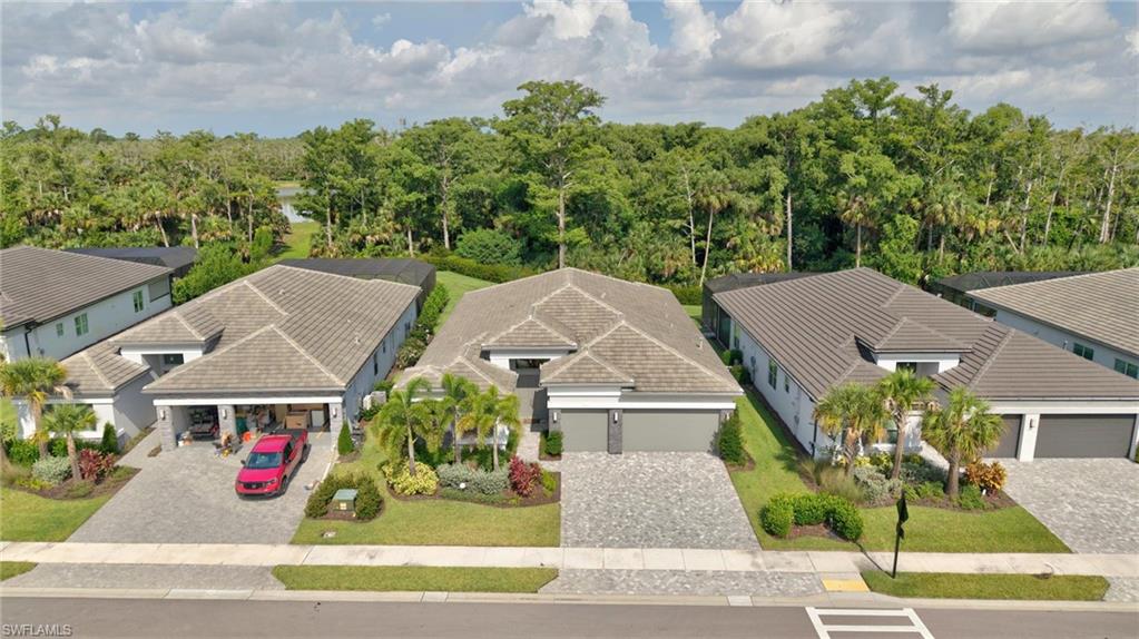 Modern dwelling with a tile roof and light-toned exterior, featuring a paver driveway, an attached garage, and manicured landscaping