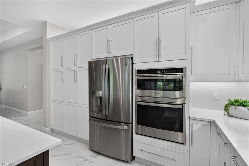 Kitchen featuring extensive white cabinetry with crown molding, stainless steel French door refrigerator, and a built-in double oven