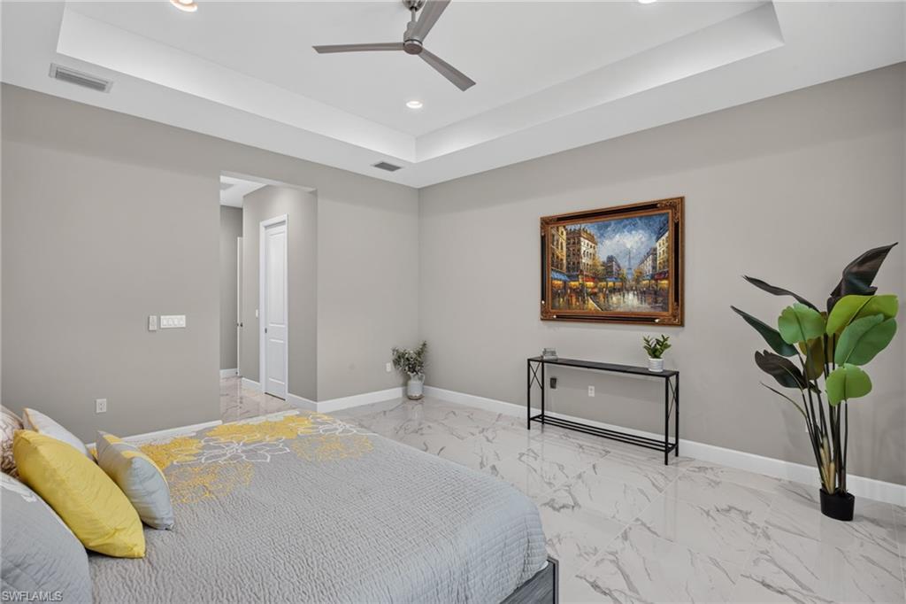 Spacious room featuring tray ceilings with recessed lighting, a ceiling fan, light gray wall tones, and large format marble-look tile flooring