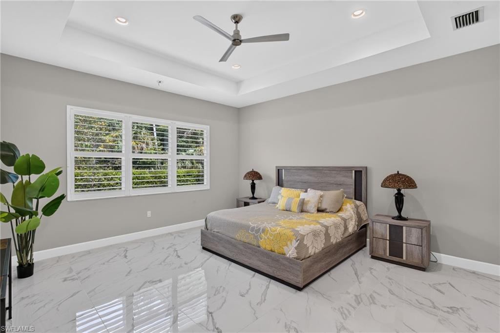 Spacious room featuring a tray ceiling with recessed lighting, a ceiling fan, and large windows with plantation shutters