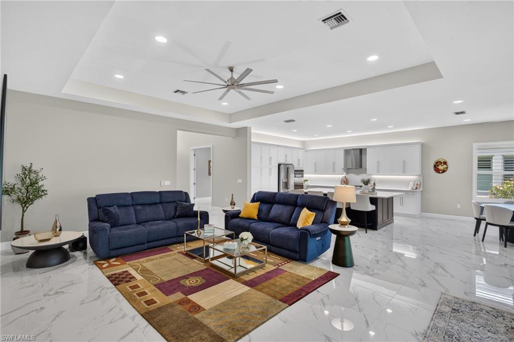 Open-concept living area featuring large format white marble-look tile flooring, tray ceilings with recessed lighting, and a modern ceiling fan