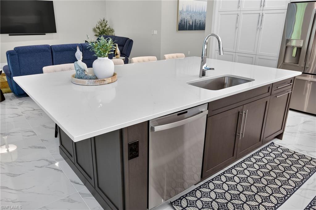 Kitchen island with a light-colored solid surface countertop, integrated stainless steel sink, and a chrome gooseneck faucet