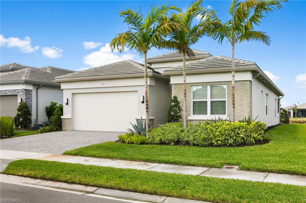 Contemporary exterior featuring a paver driveway, an attached garage, a tiled roof, mature palm trees, and manicured landscaping