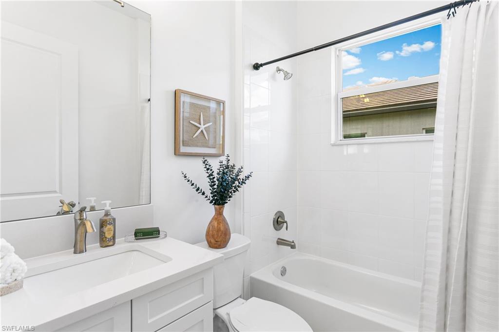 White bathroom featuring an integrated sink vanity with a light-toned countertop, a full-length mirror, a window-equipped tub/shower combination, and white tile surround