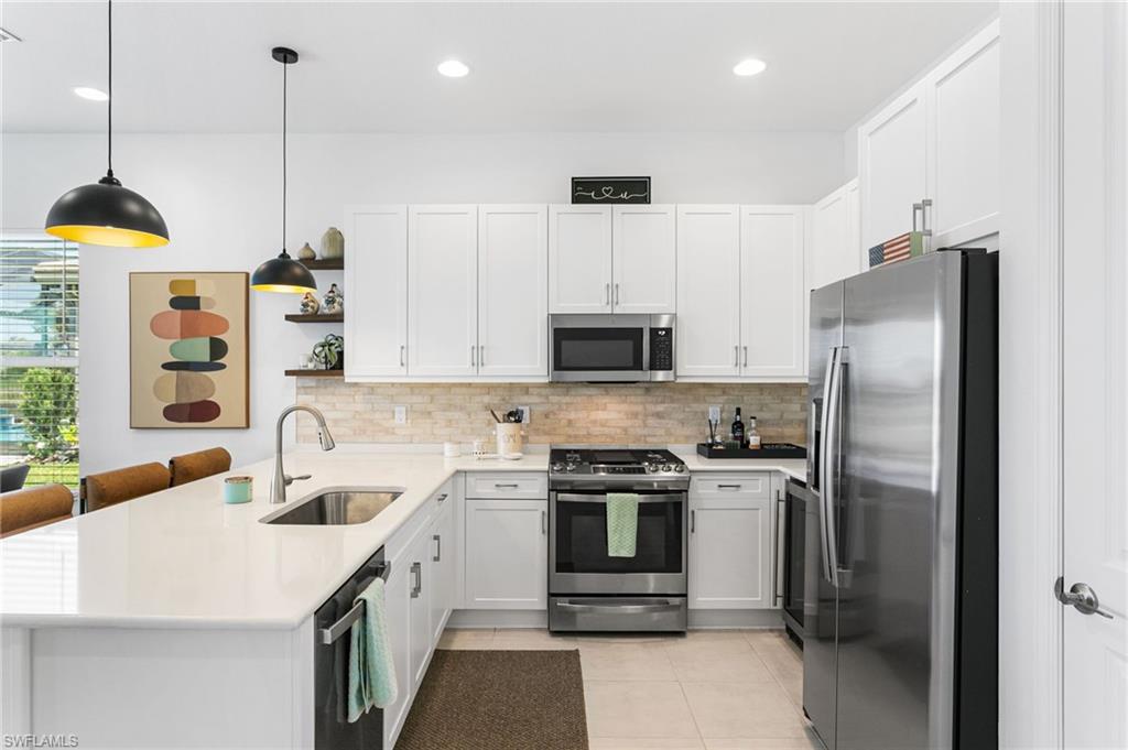 Kitchen featuring white shaker-style cabinetry, stainless steel appliances, a stone tile backsplash, and a large central island with a sink