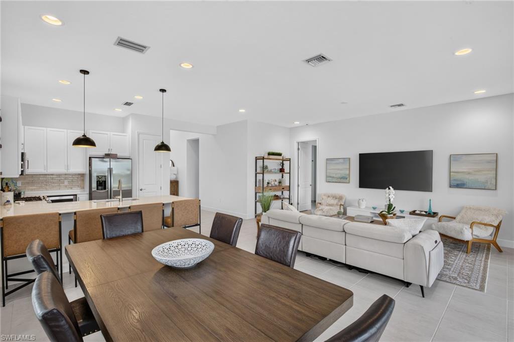 Open-concept living space featuring a spacious dining area, a contemporary kitchen with white cabinetry, a large kitchen island with seating, a stainless steel refrigerator, and recessed lighting throughout