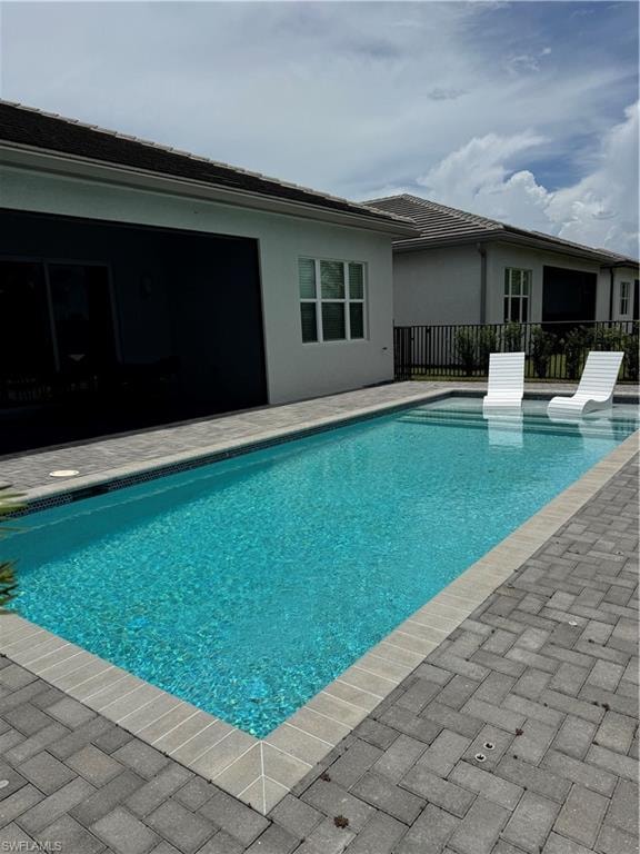 Expansive outdoor living area featuring a rectangular swimming pool with integrated tanning ledge, paver patio, screened lanai, and tile roof