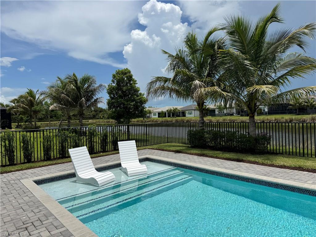Swimming pool featuring an integrated sun shelf with steps, paver decking, and a black wrought-iron style fence