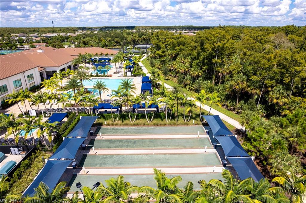 Community amenity area featuring a large clubhouse, multiple swimming pools, bocce ball courts, and extensive landscaping with mature palm trees