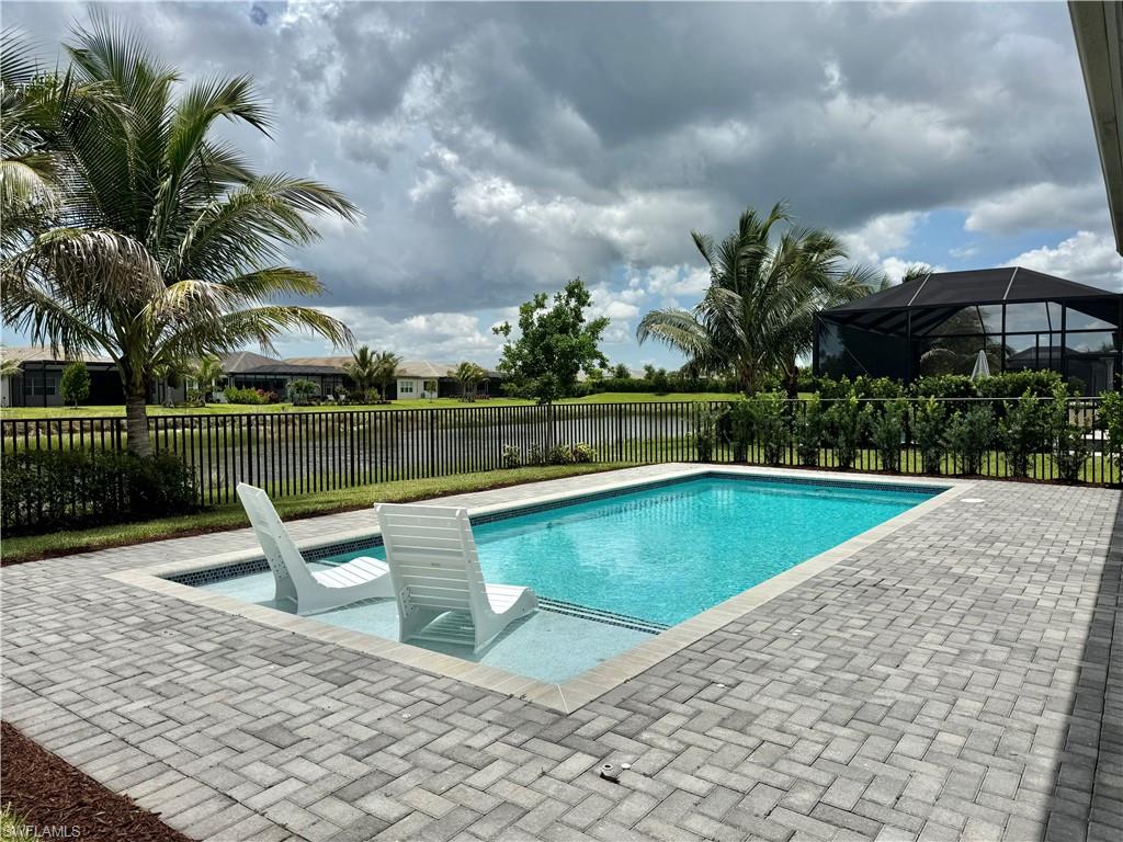 Backyard oasis featuring a rectangular swimming pool with an integrated sun shelf, surrounded by paver patio decking