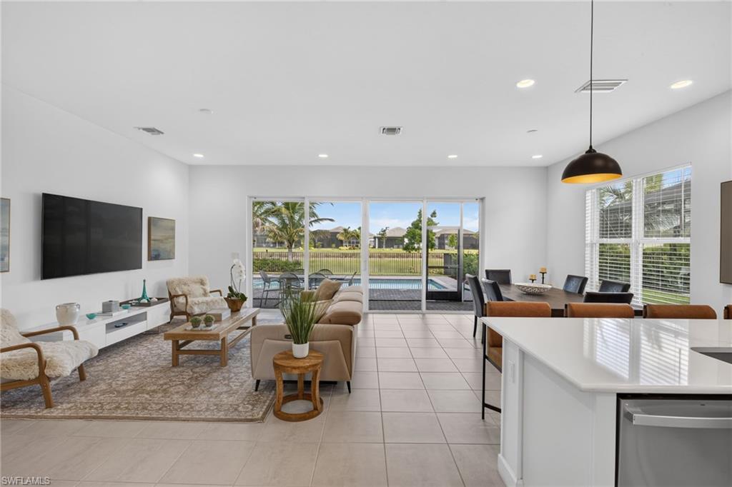 Open-concept living space featuring large format tile flooring, recessed lighting, and expansive sliding glass doors opening to a screened lanai with a pool and water views