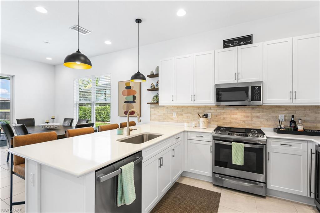 Contemporary kitchen featuring white cabinetry, stainless steel appliances, a light-toned brick pattern backsplash, and a large island with an undermount sink