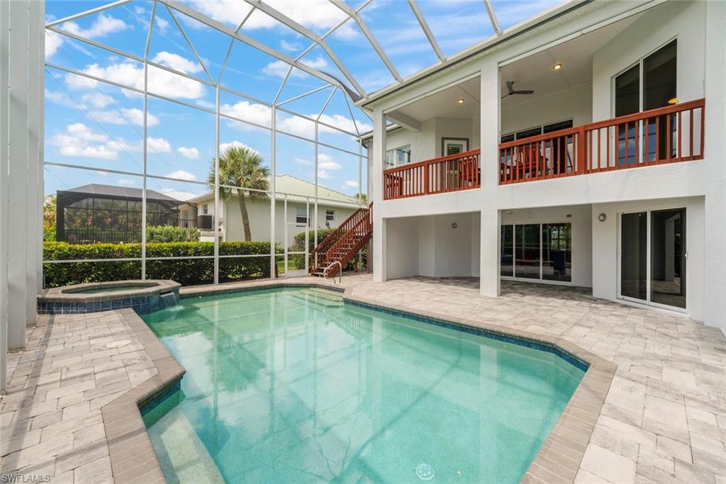 Screened-in pool area featuring a rectangular pool with integrated spa and waterfall feature, surrounded by paver decking