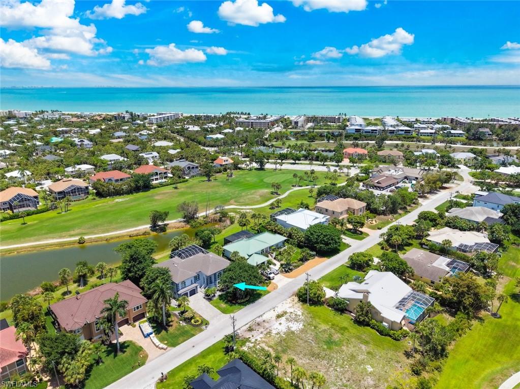 Aerial perspective showcasing a residential neighborhood with verdant landscaping, offering proximity to a golf course, a body of water, and the distant ocean