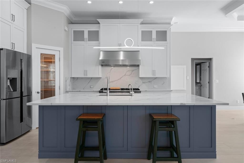 Gourmet kitchen featuring a large central island with a quartz countertop, stainless steel appliances, white cabinetry with glass inserts, and a decorative pendant light fixture