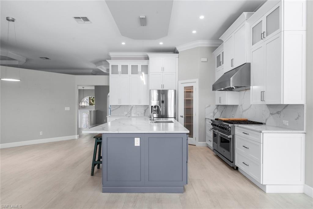 Modern kitchen featuring a large central island with a contrasting base, white shaker-style cabinetry, stainless steel appliances, marble-look countertops and backsplash, and recessed lighting