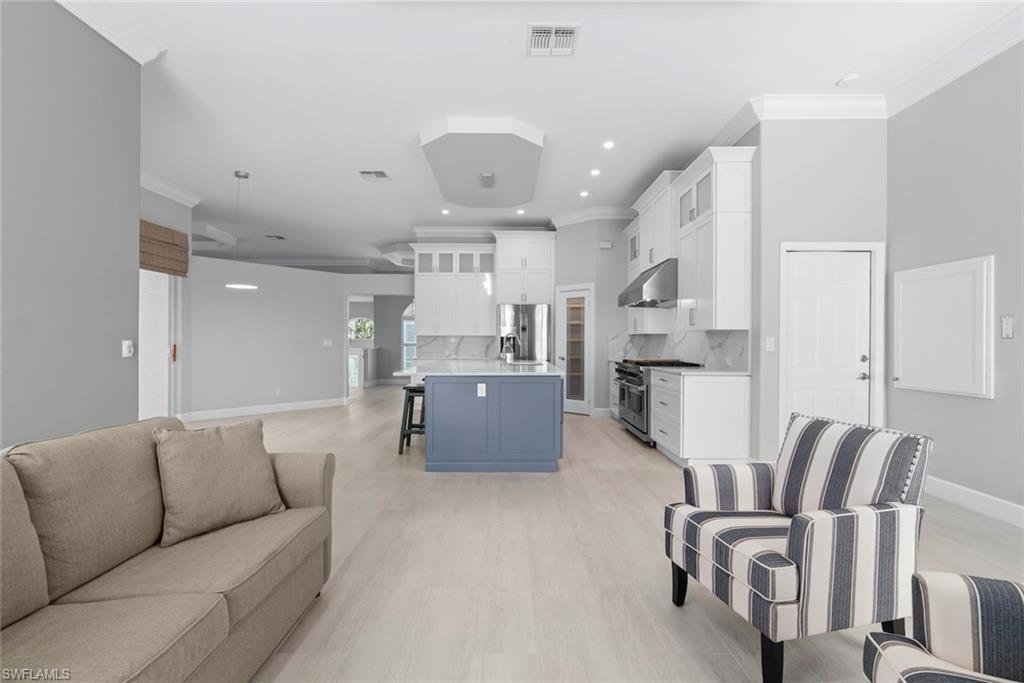 Open-concept living area featuring light wood-finish flooring, recessed lighting, and crown molding