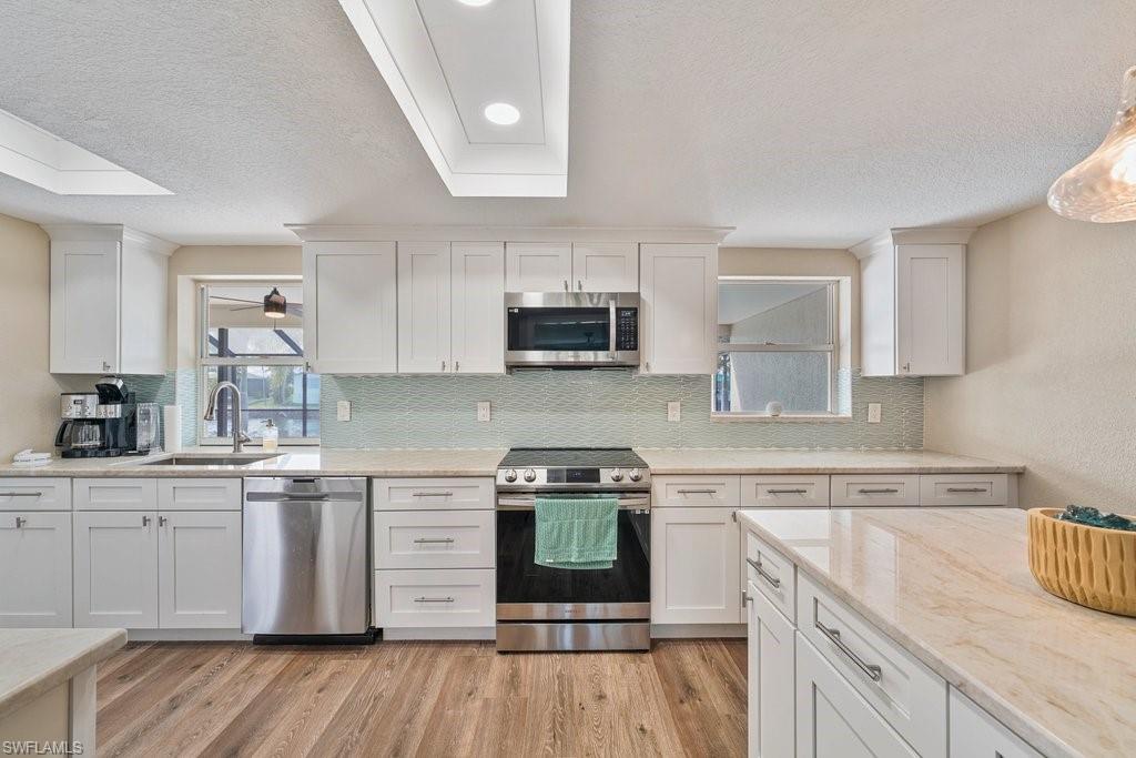 Modern kitchen featuring white shaker cabinetry, stainless steel appliances, light-toned countertops, a light blue mosaic tile backsplash, and wood-finish flooring