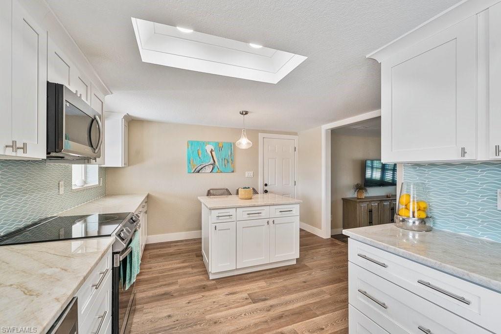 Kitchen featuring white shaker cabinetry, light-toned countertops, wave-patterned blue backsplash, stainless steel appliances, and a central island