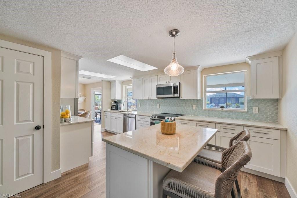 Well-appointed kitchen featuring wood-finish flooring, white cabinetry, integrated stainless steel appliances, a light-toned countertop, and a tiled backsplash